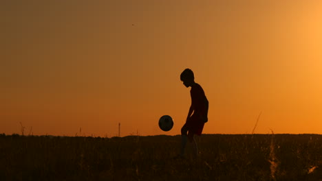 A-young-young-boy-football-player-trains-playing-with-a-ball-stuffing-on-his-leg-at-sunset-in-slow-motion-during-the-Golden-hour-in-the-field-until-sunset.-Training-from-dusk-to-dawn.-Concept-path-to-success
